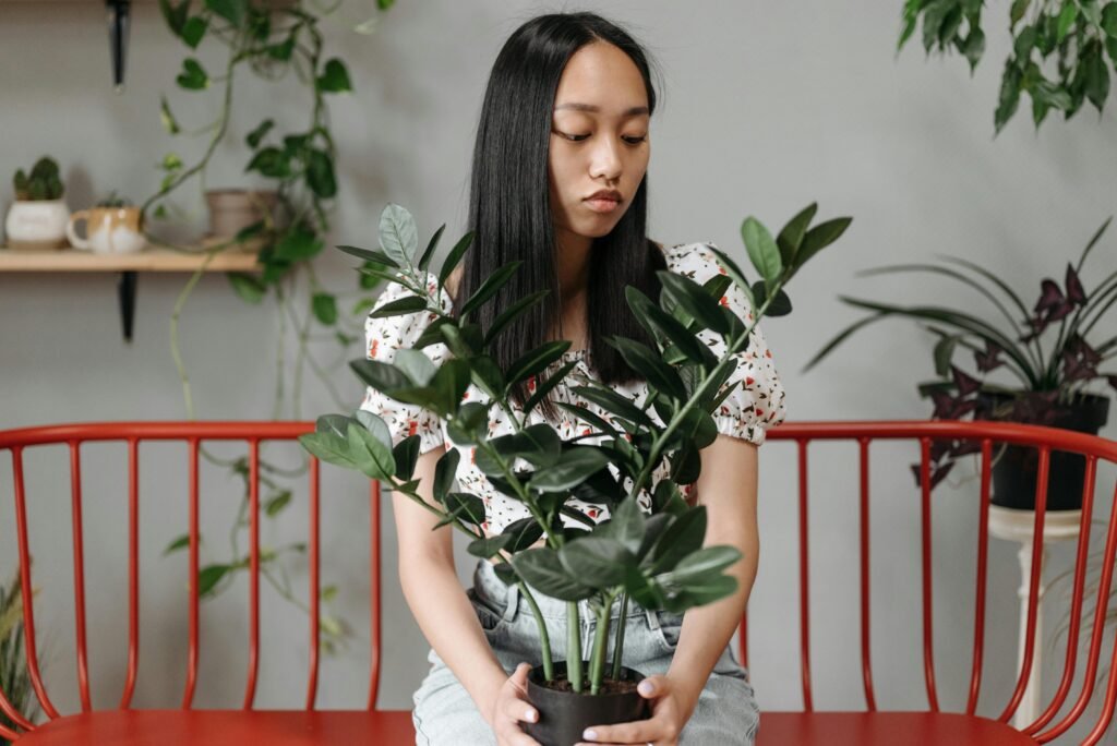 Asian woman sitting thoughtfully on a red bench indoors, holding a potted plant.